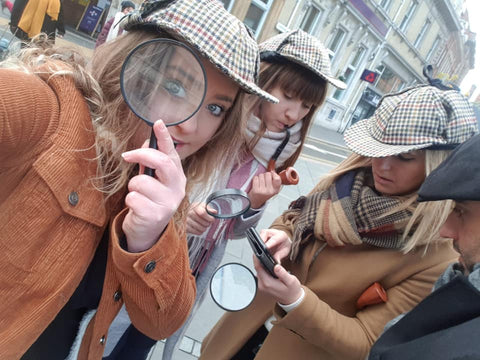 A group of detectives outdoors at a corporate event in the UK. There are three people in the image and one is looking through a magnifying glass at the camera.