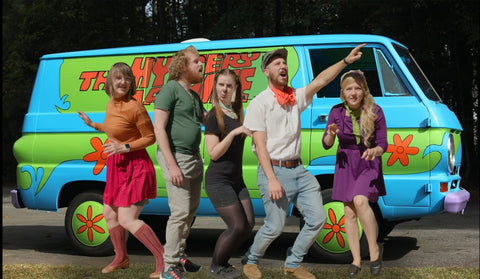At an outdoor event in the USA, this group is dressed as the gang from Scooby Doo. They have a mystery machine bus and are posing as in the cartoon.