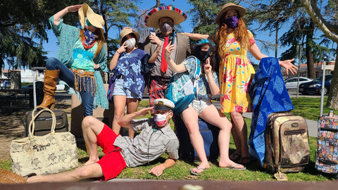 A group of mask wearing colleagues at an team event in the USA. They are wearing tropical shirts, straw hats and are posing for the camera.