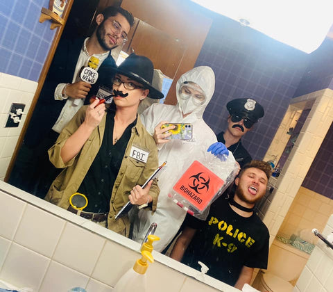 A team of detectives ready to take on the mystery. They are taking a photo in a mirror and are dressed in a variety of detective inspired costumes.