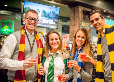 At a Witchcraft & Wizardry themed socially distanced team building event, this group are dressed in Harry Potter outfits and are having their photo taken in a bar or restaurant.