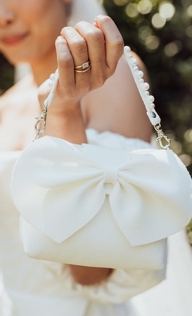Bride holds wedding bag with big bow and pearl detail