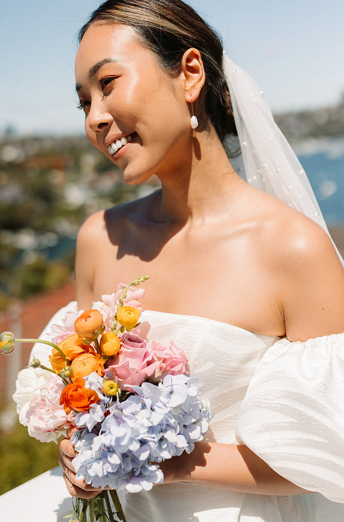 Bride wearing a wedding dress, pearl earrings holding a rainbow garden style bouquet