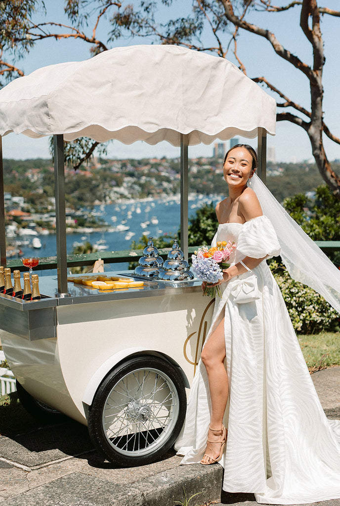 Bride stands next to granita cart in the sun 