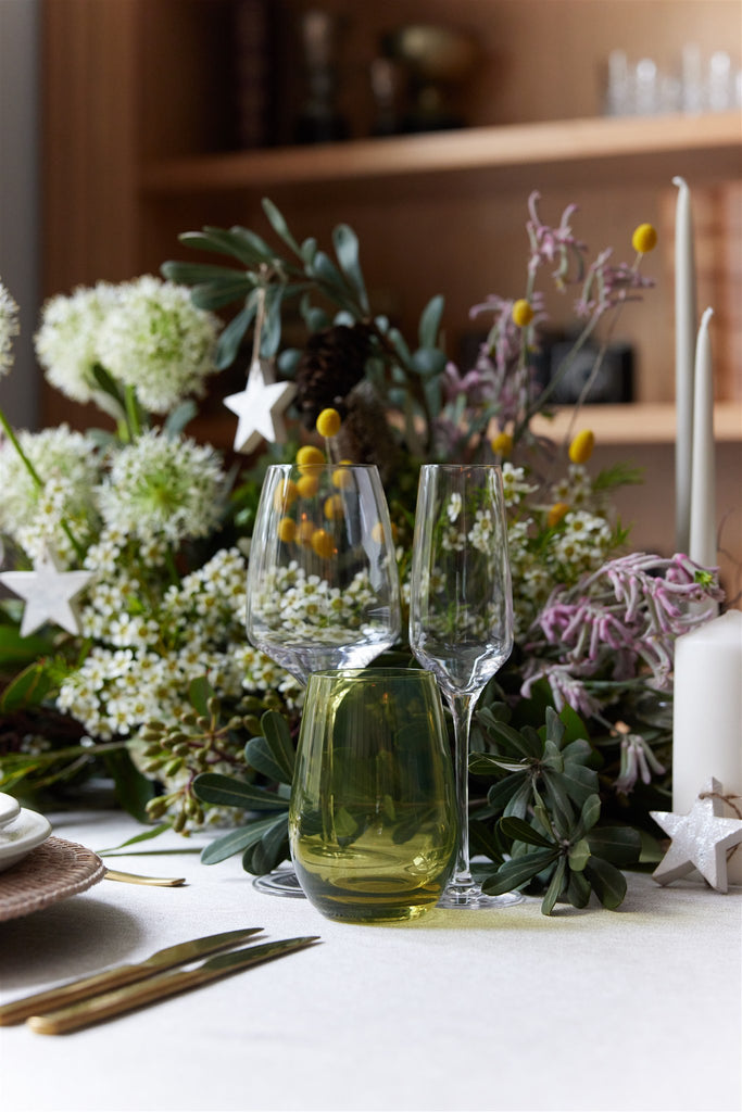 Close up image of a floral table centrepiece with green and purple florals and green glassware 