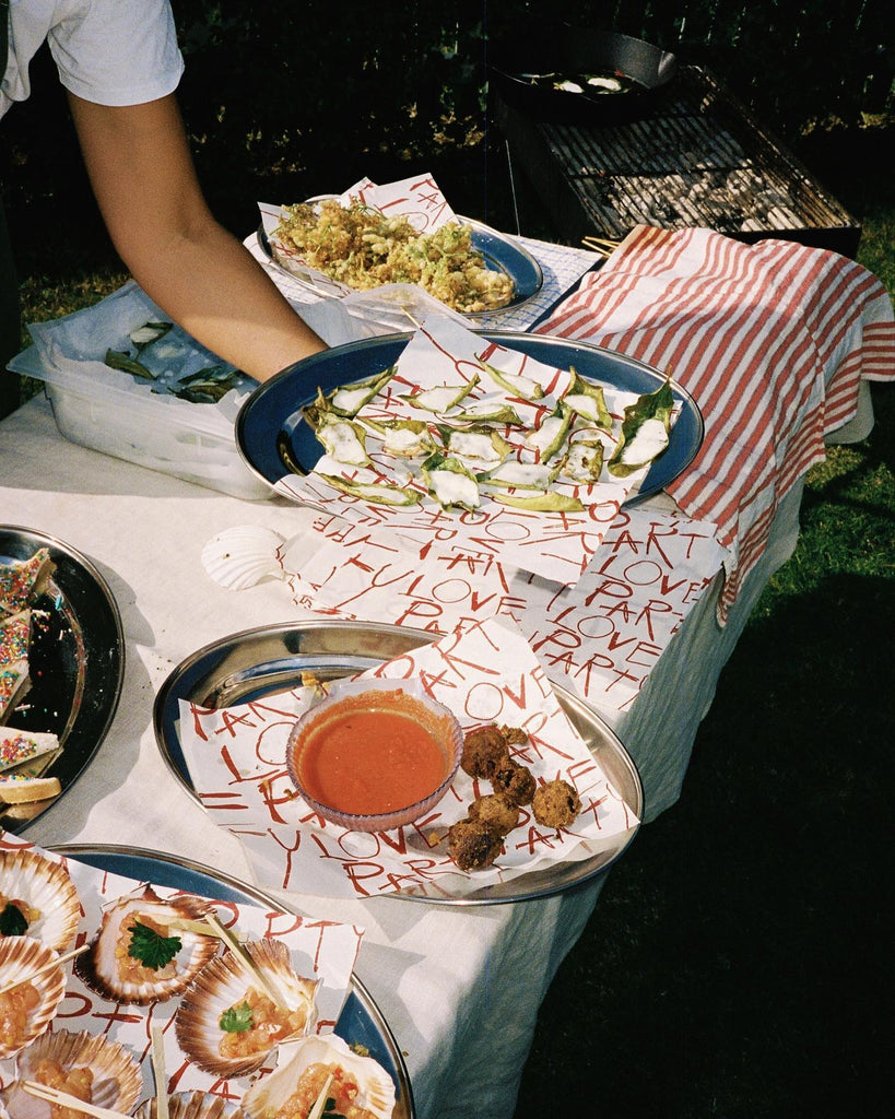 Plates of food lay on silver platters with love party hand written across paper 