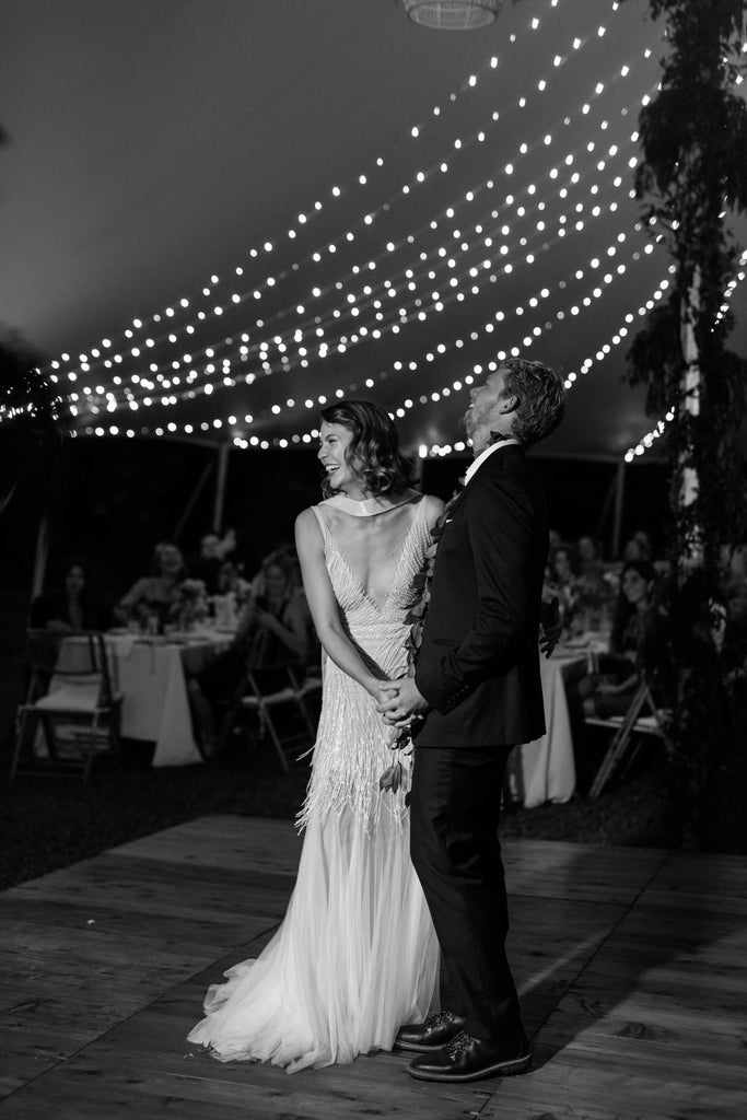 Bride and Groom stand on the dance floor of their reception smiling under a canopy of fairy lights 