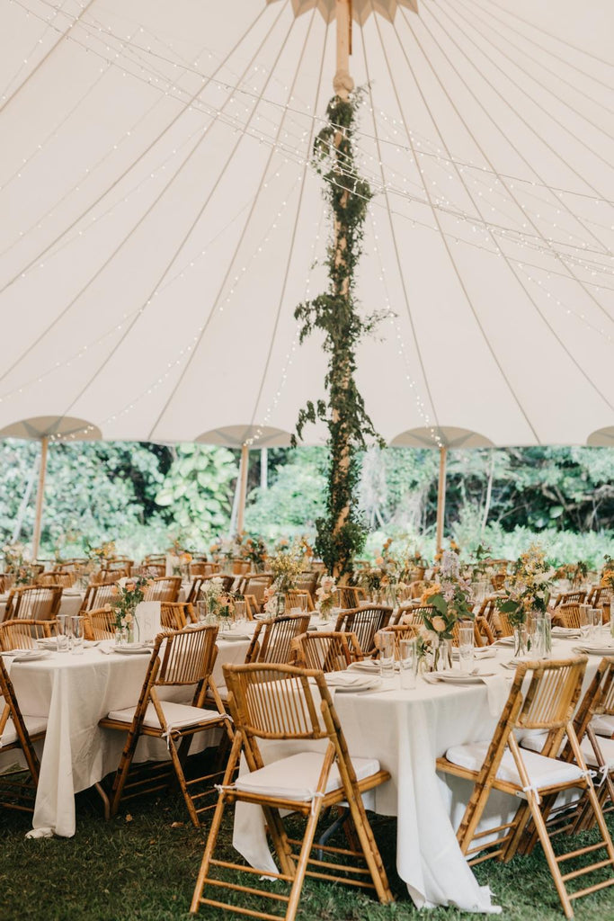 A white tent style marquee is decorated with long tables, bamboo chairs and greenery 