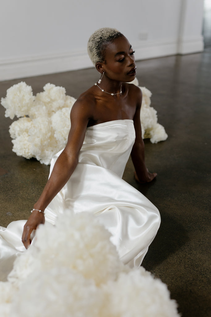 Bride wearing strapless gown and pearl accessories sits amongst en masse floral installation 