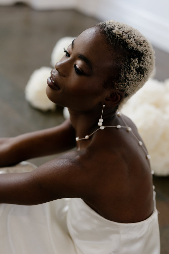 Bride sits wearing bridal pearl earrings and long pearl necklace 