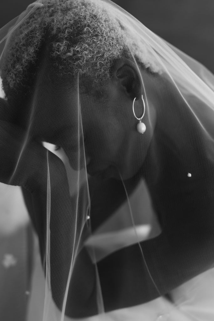 Bride wears a hoop earring with pearl drop, looking down with veil over her head. 