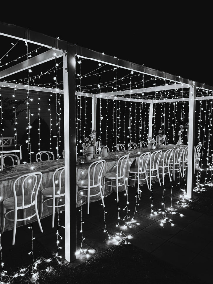 A canopy of fairy lights are hung as a tunnel above a long table decorated for a wedding reception 