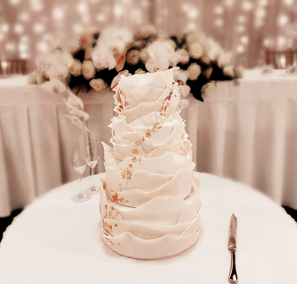 White wedding cake with ruffle like texture is displayed on a round white table 