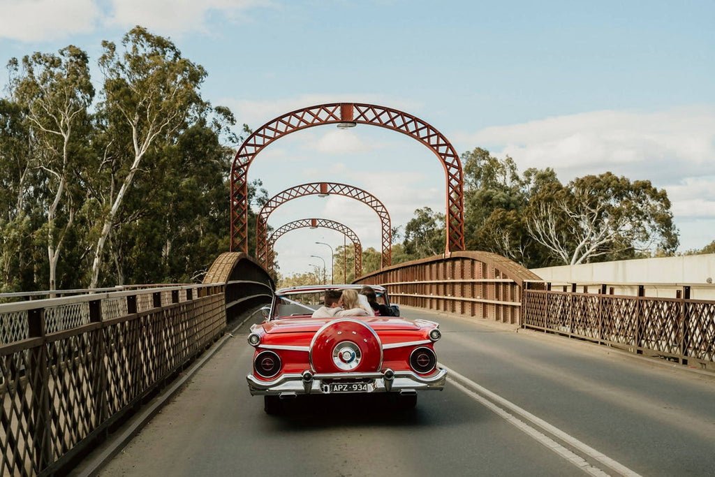 Bride and groom driving away in a red vintage convertible 