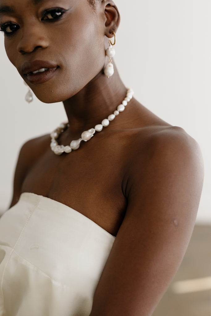 Bride looks at camera wearing earring with two large pearls and a chunky pearl chocker necklace. 