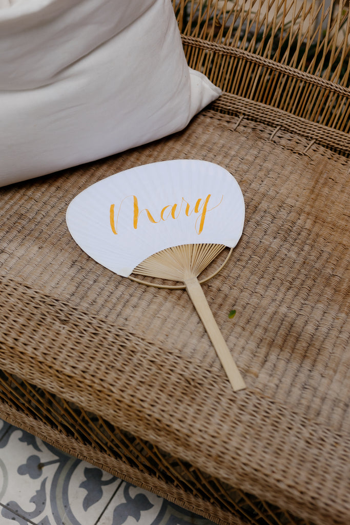 Personalised calligraphy fan sit on chair in wedding courtyard