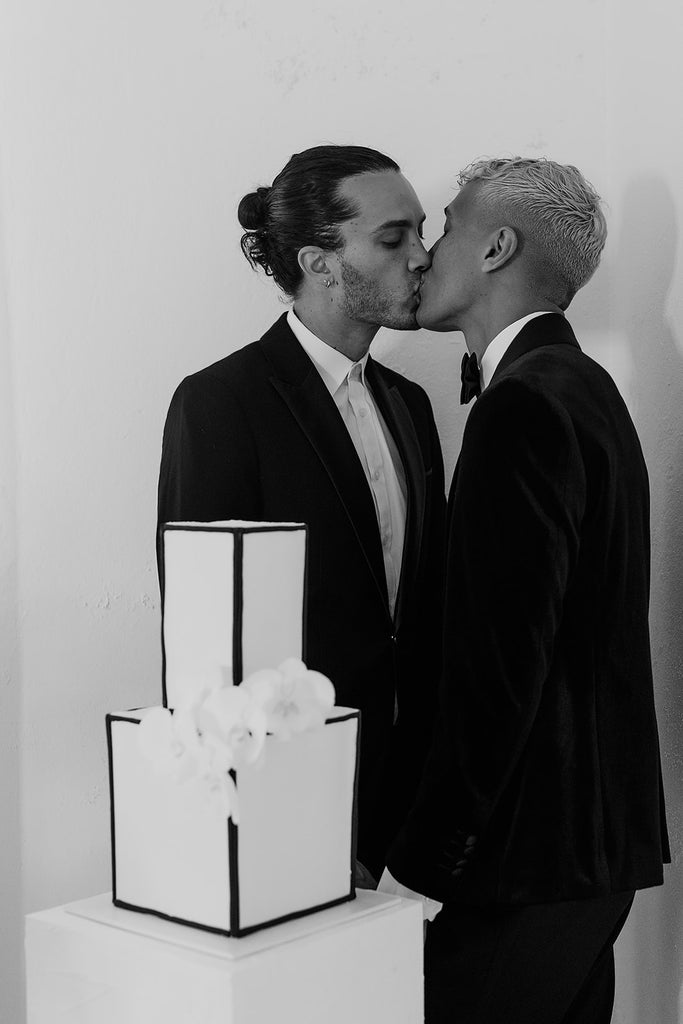Couple kisses behind monochrome wedding cake.