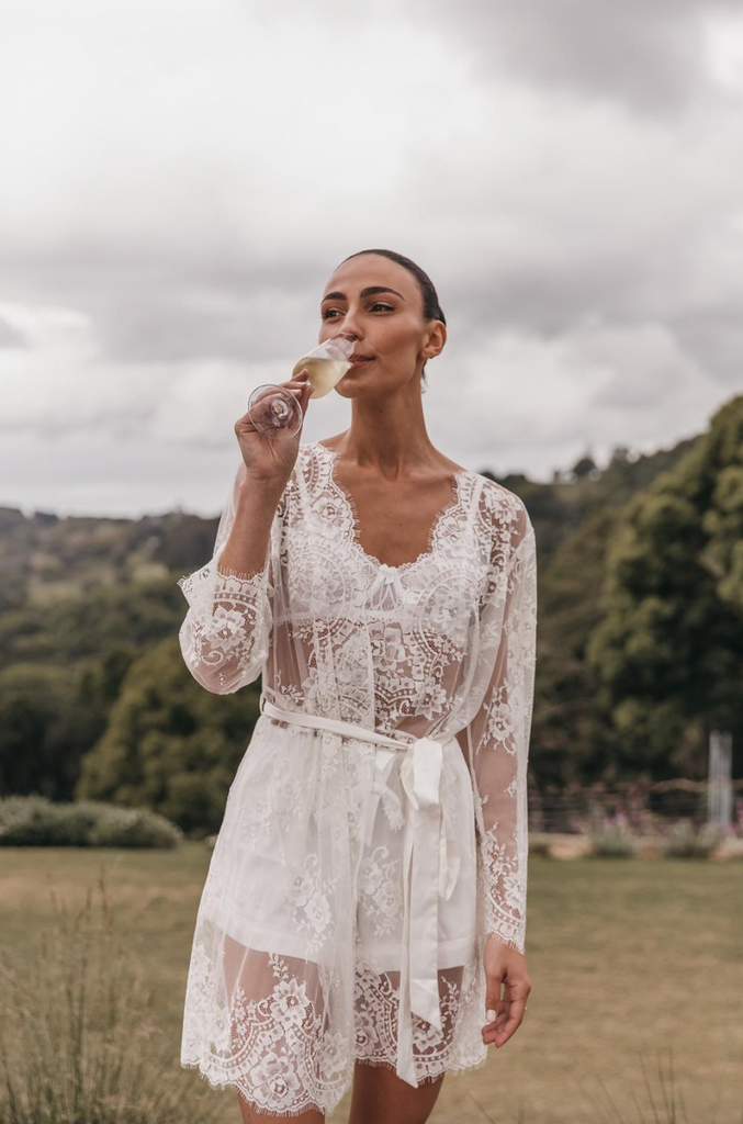 Tayla Damir on her wedding day wearing bridal robe and drinking champagne with a hinterland backdrop