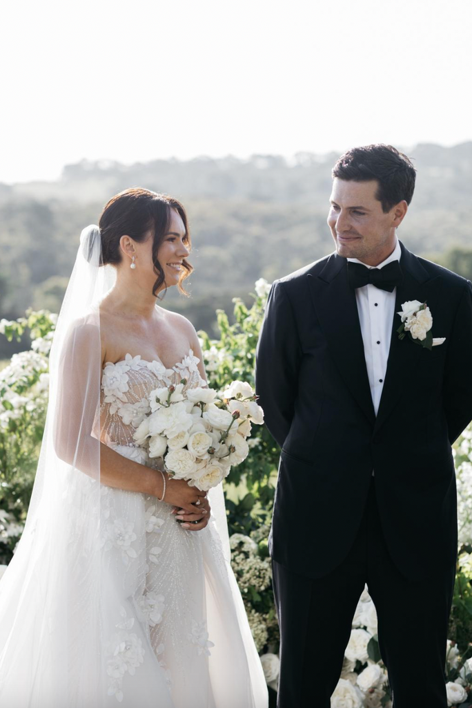 Victoria Devine and Husband Stephen Morris at their wedding ceremony at Jackalope in the Mornington Peninsula. Groom smiles at Bride. Bride is holding a classic bouquet of white roses. 