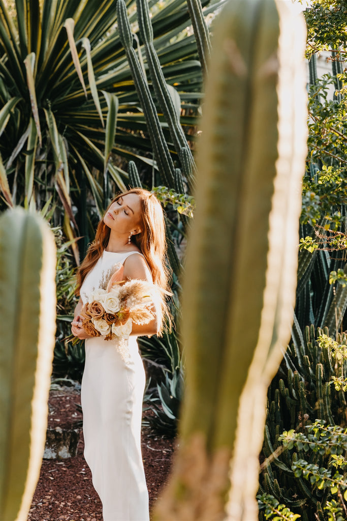 Bride stands in the sun in a garden full of cactus.