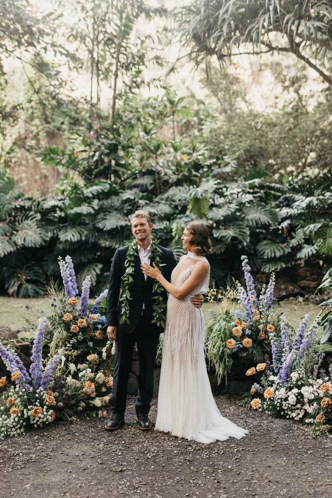 Bride and Groom are photographed at the head of the aisle surrounded by tropical greenery and colourful floral arrangements  