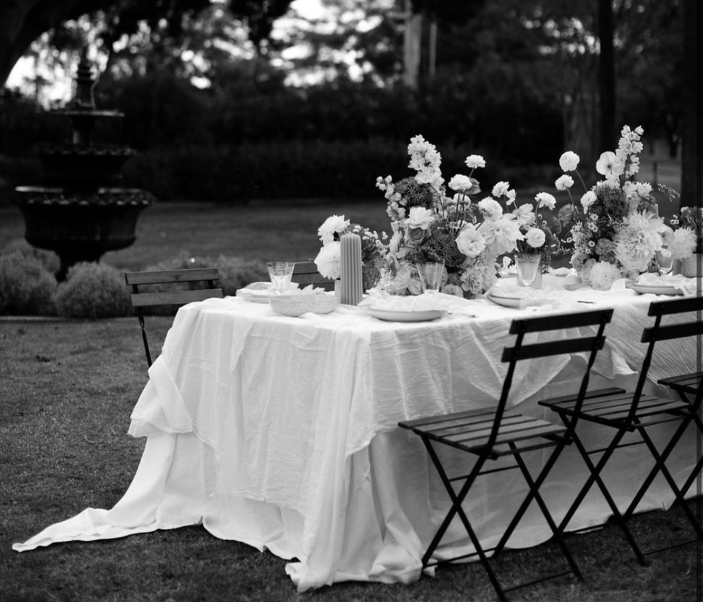 Black and white image of table set in a garden.