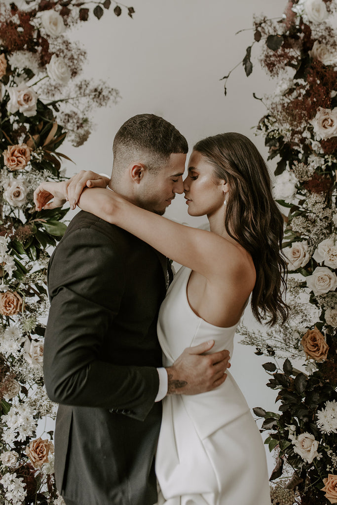 bride and groom embrace and kiss in front of blush and nude flowers