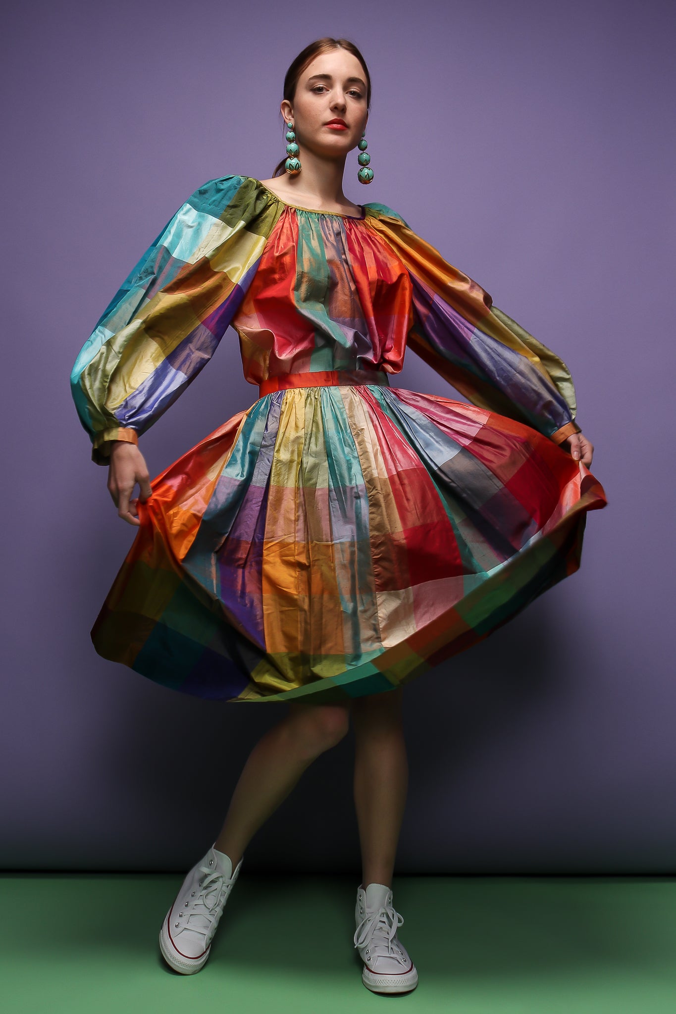 girl in rainbow silk Carledi balloon sleeve top & skirt & drop earrings on purple at Recess LA
