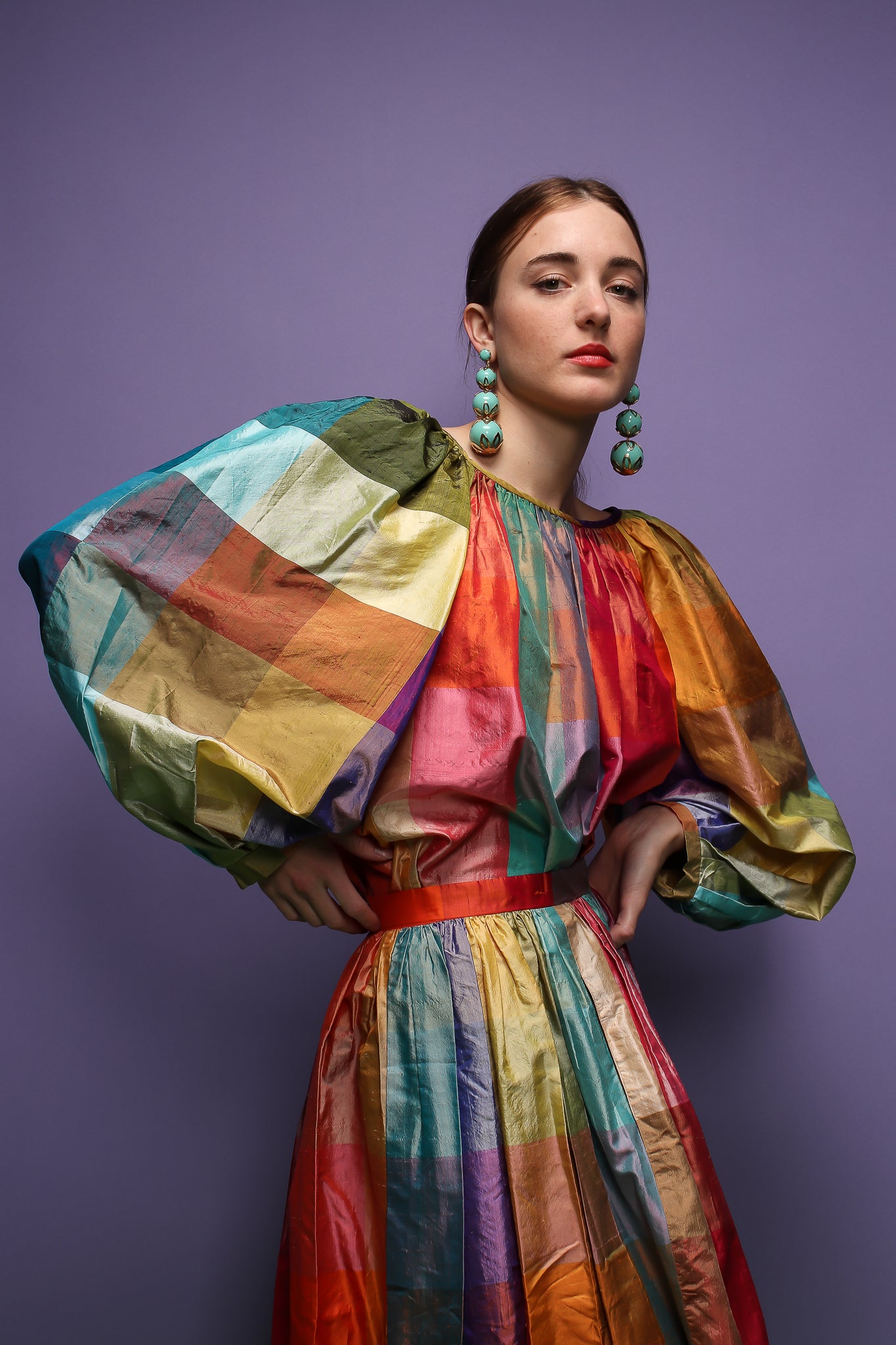 girl in rainbow silk Carledi balloon sleeve top & skirt & drop earrings on purple at Recess LA