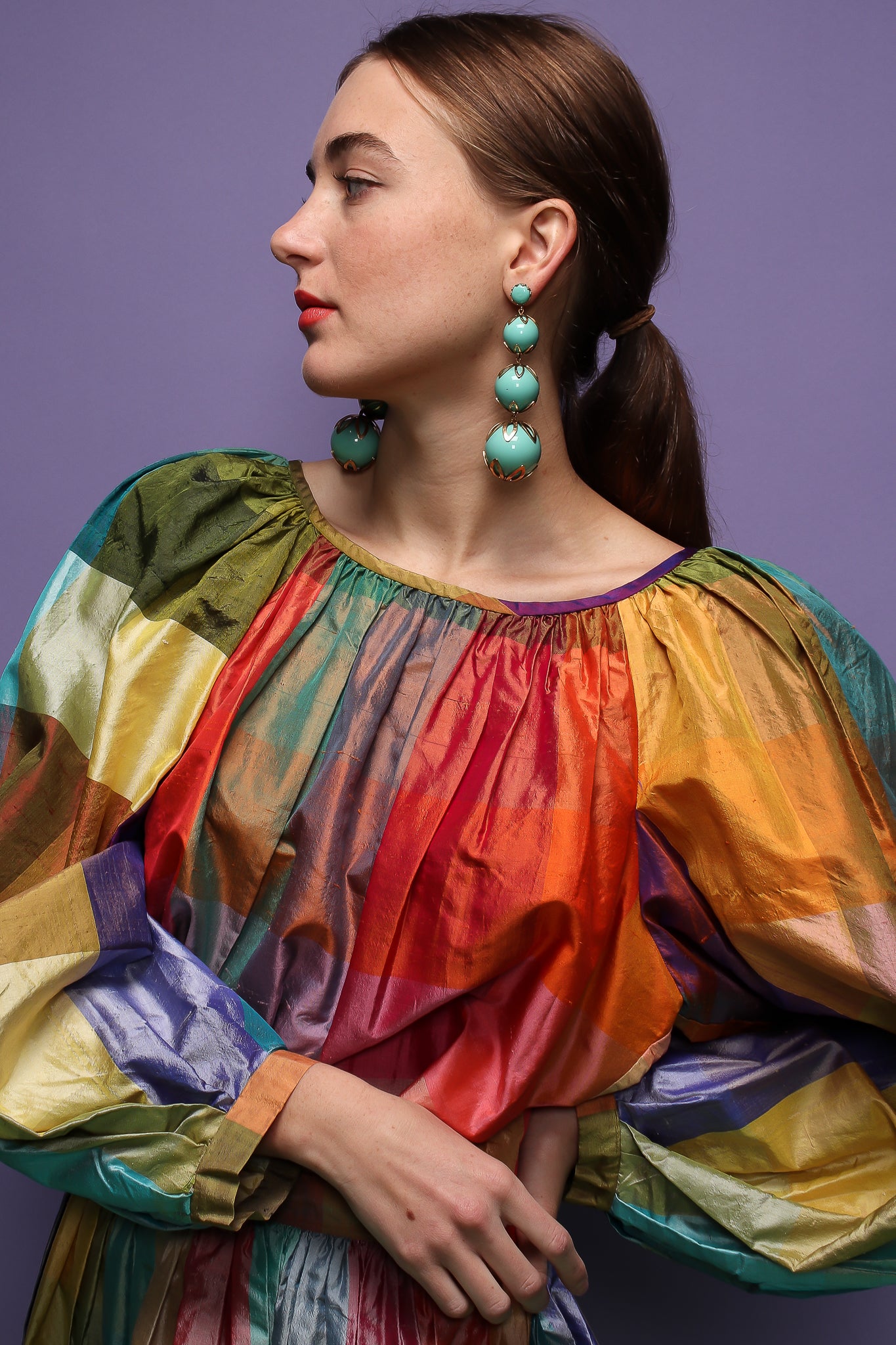girl in rainbow silk Carledi balloon sleeve top & skirt & drop earrings on purple at Recess LA