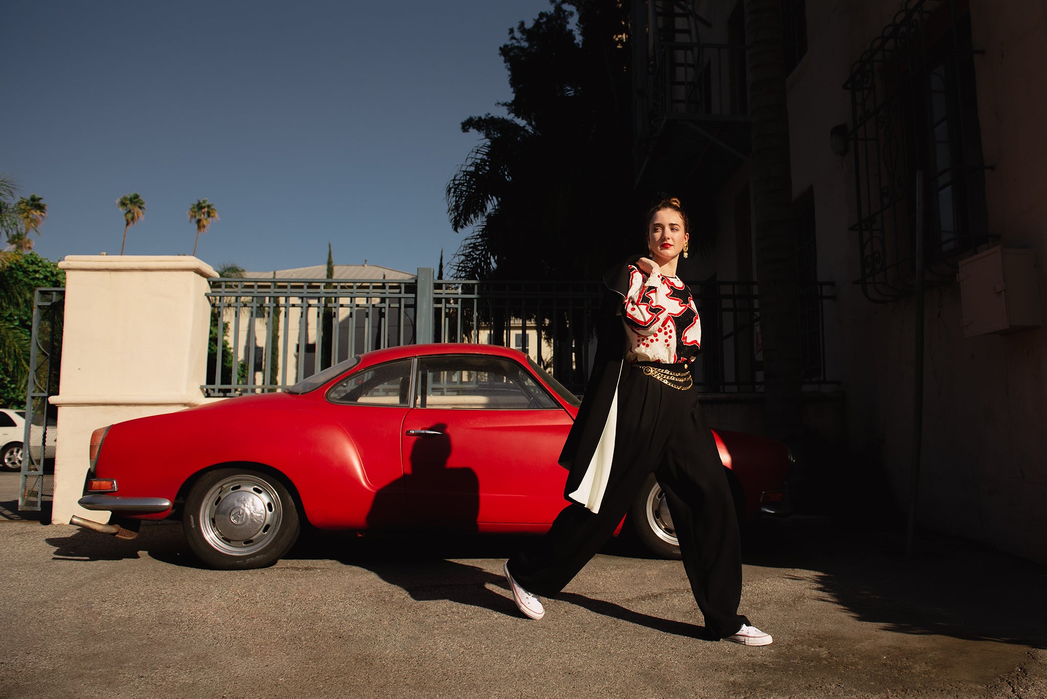 Girl wearing Recess vintage Sonia Rykiel cape and pant set and red print blouse in front of red car