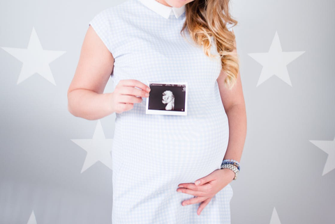 A pregnant woman holding up an ultrasound photo.