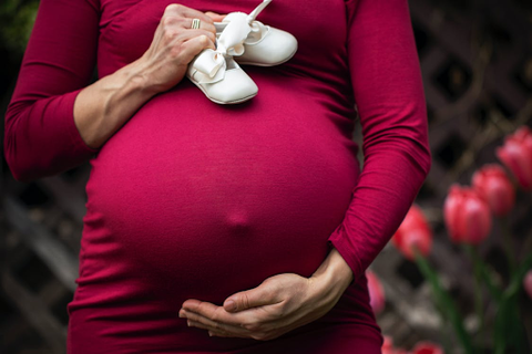 A woman holding her pregnant stomach and a small pair of baby booties.