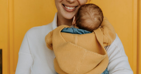 woman holding a baby in a yellow knitted sweater against a yellow wall