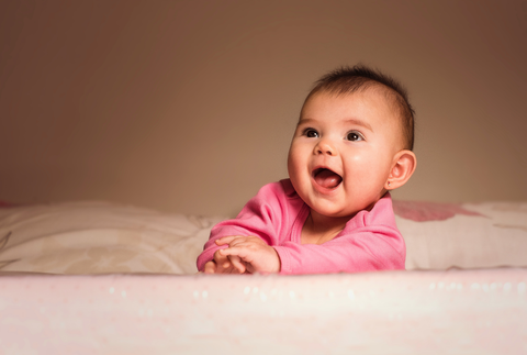  baby in a pink onesie looking up and laughing