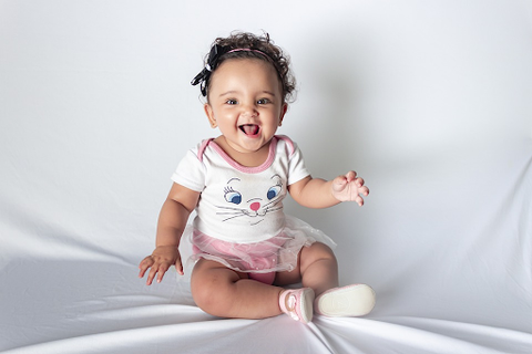 a baby in a white and pink cat onesie laughing against a white background