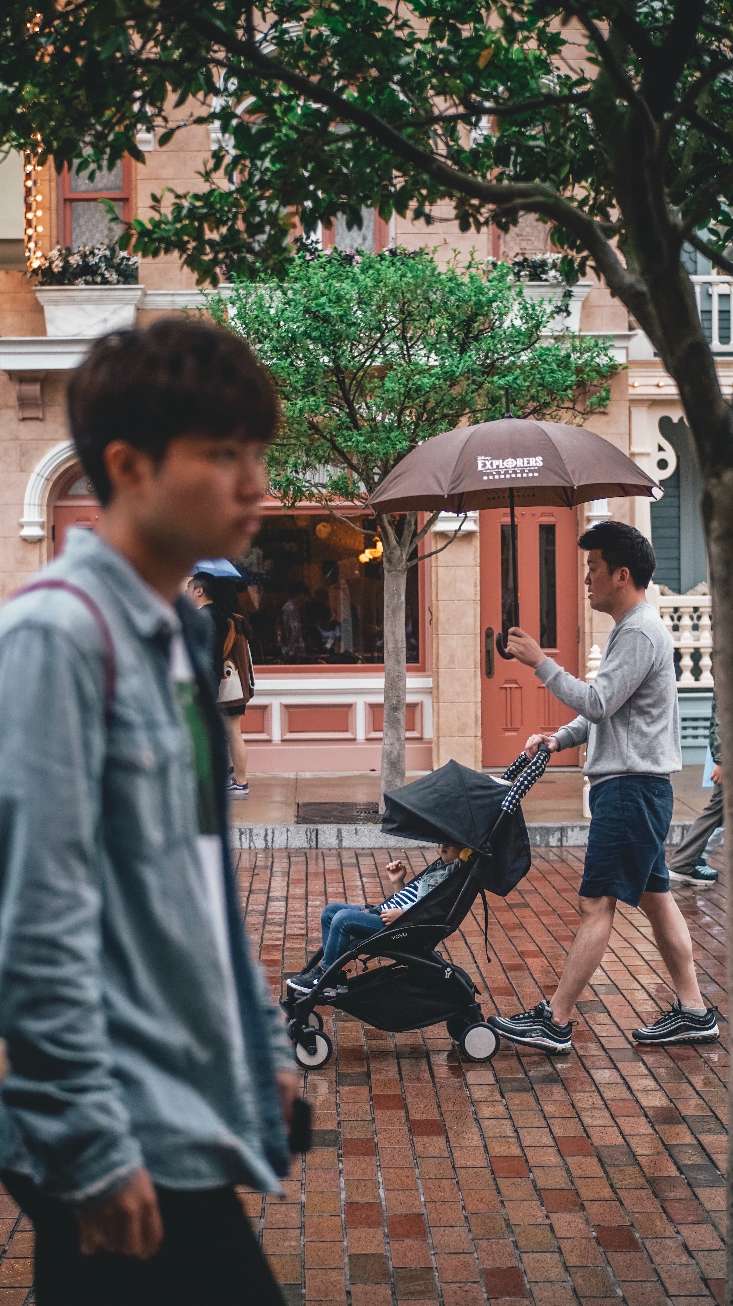 man with umbrella walking a baby in an umbrella stroller
