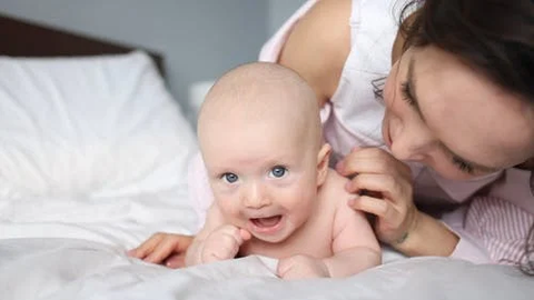 mother playing with her laughing baby on a bed