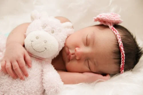 baby with a pink hairband sleeping with a toy