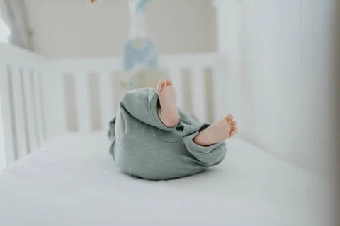 baby in a blue onesie rolling in a crib