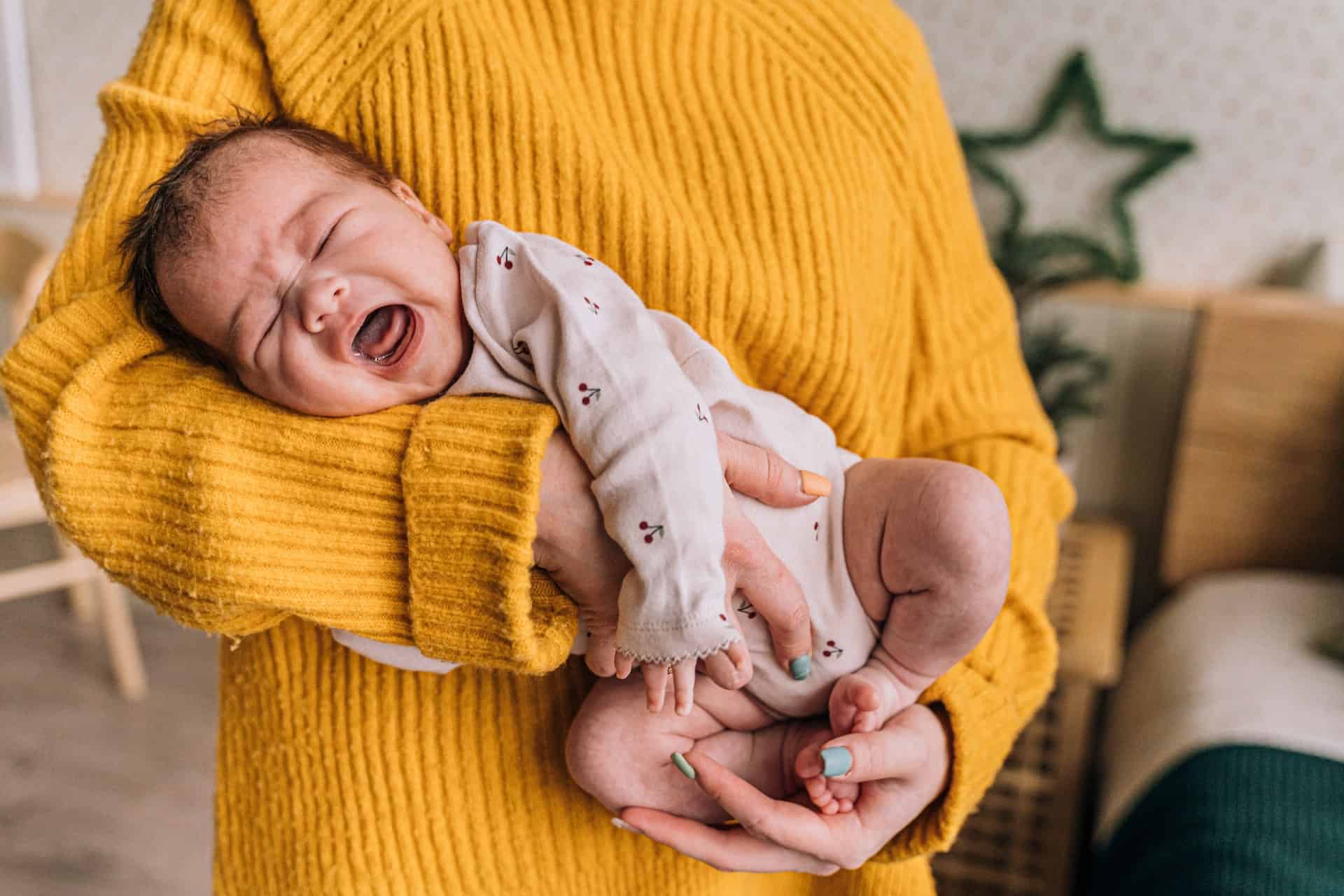 A parent in a yellow sweater holding their crying baby