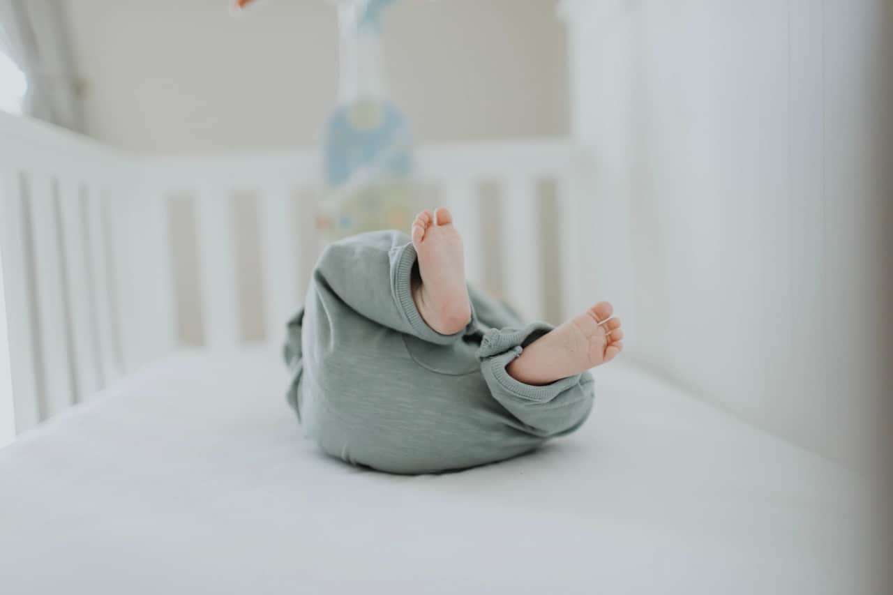 a baby in a teal onesie rolling in a crib