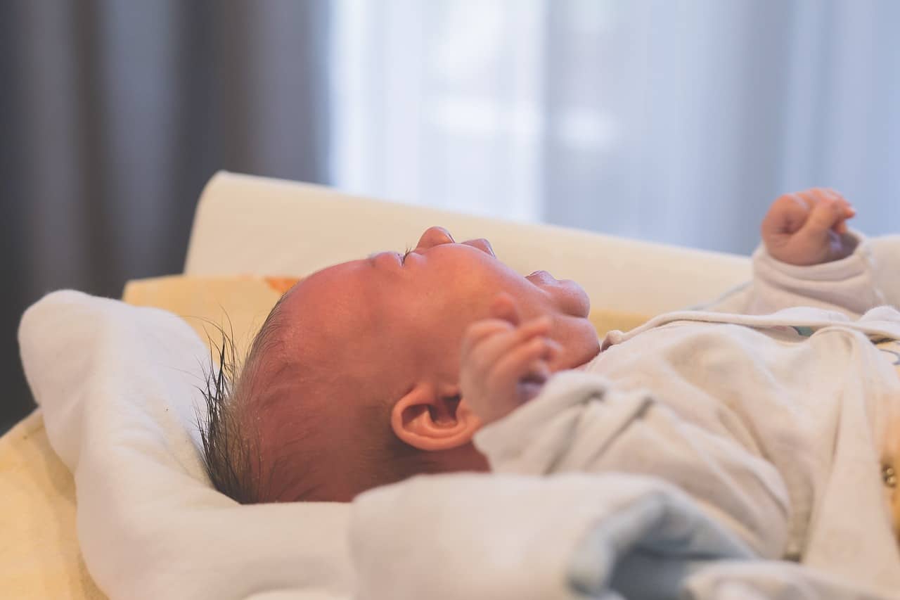 baby in a white onesie crying against a blanket