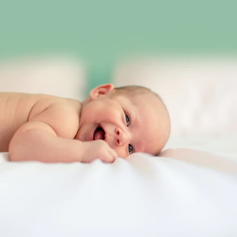 A baby laying on its stomach looking at the camera.