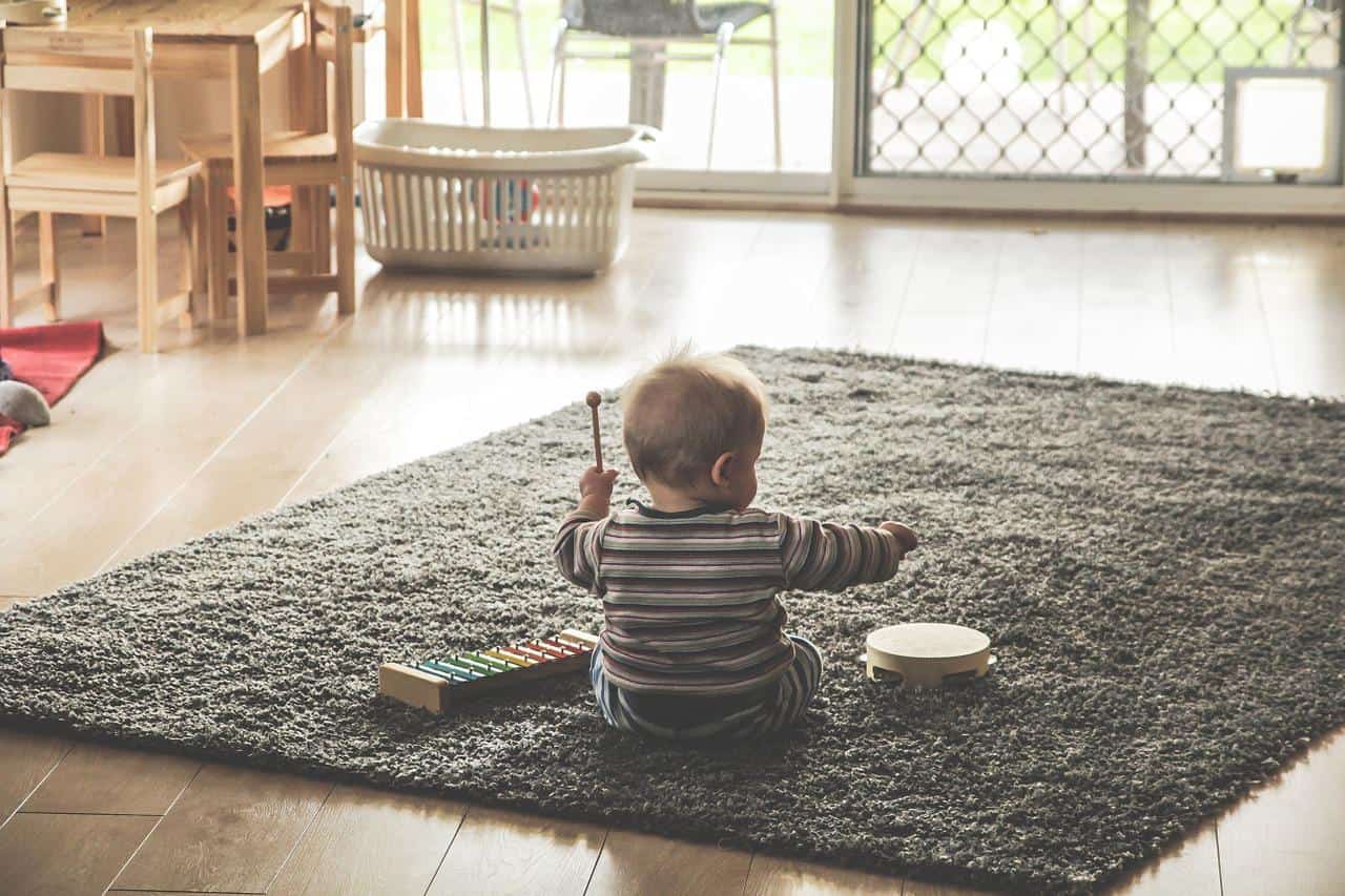 Baby sitting on a gray rug and playing with wooden toys