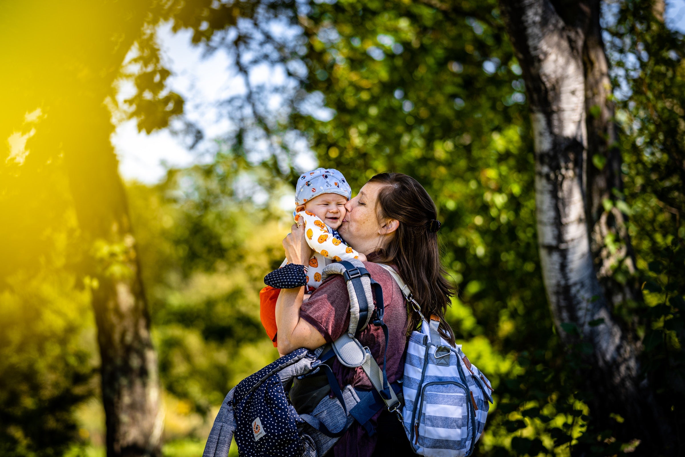 mother kissing her baby in nature while carrying a breast pump bag