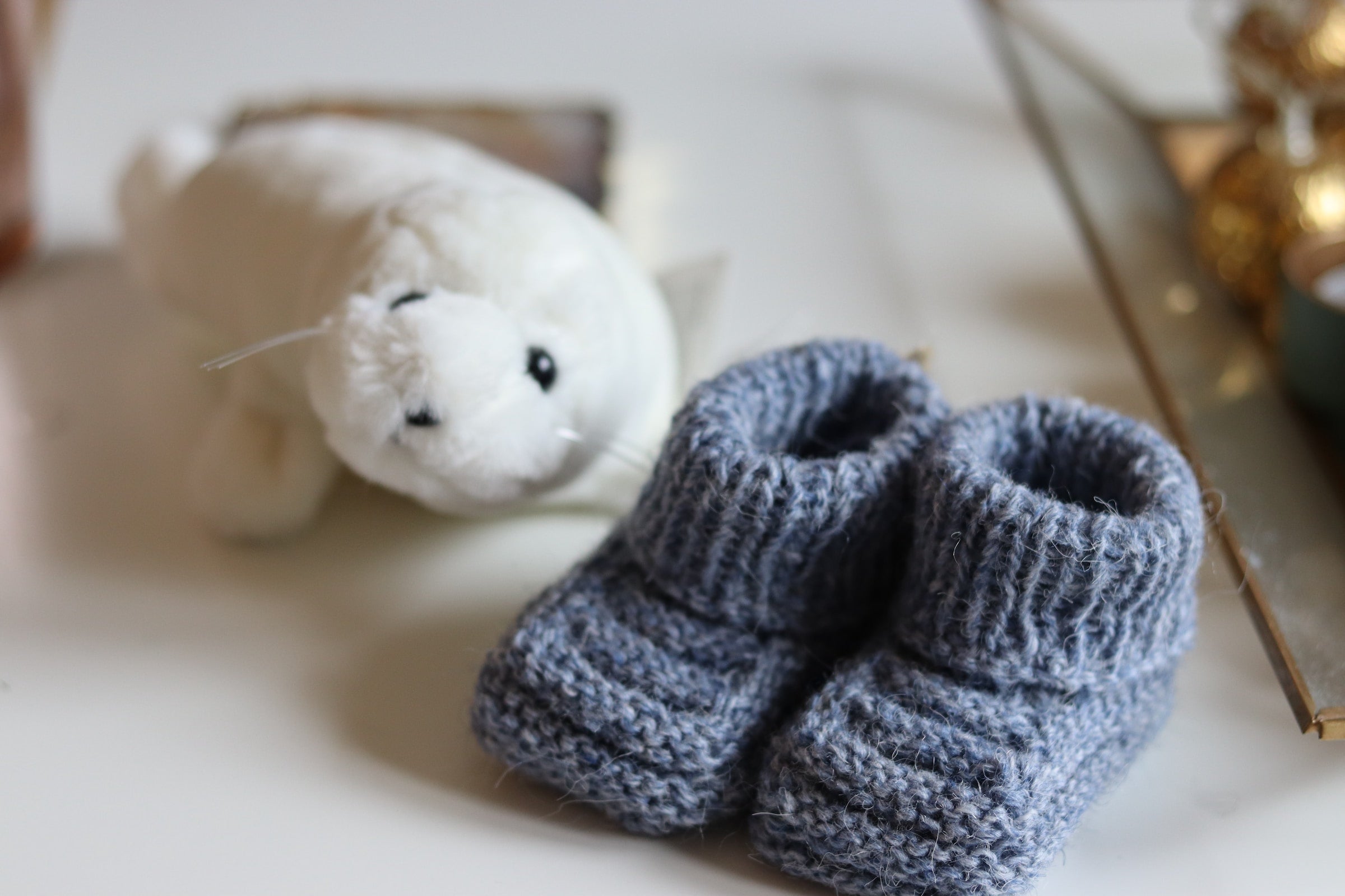 A plush toy seal sits next to a pair of knitted baby booties.