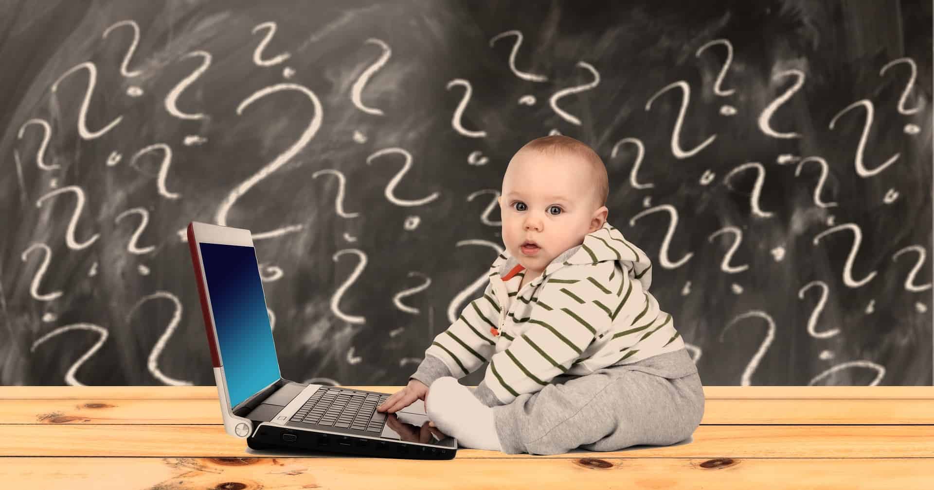Infant sitting at a laptop with question marks behind him