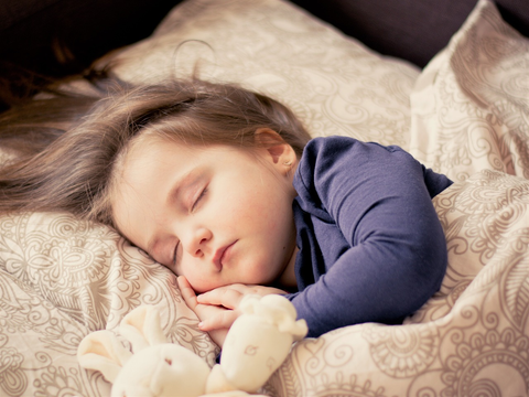 A little girl sleeping with her stuffed bear.
