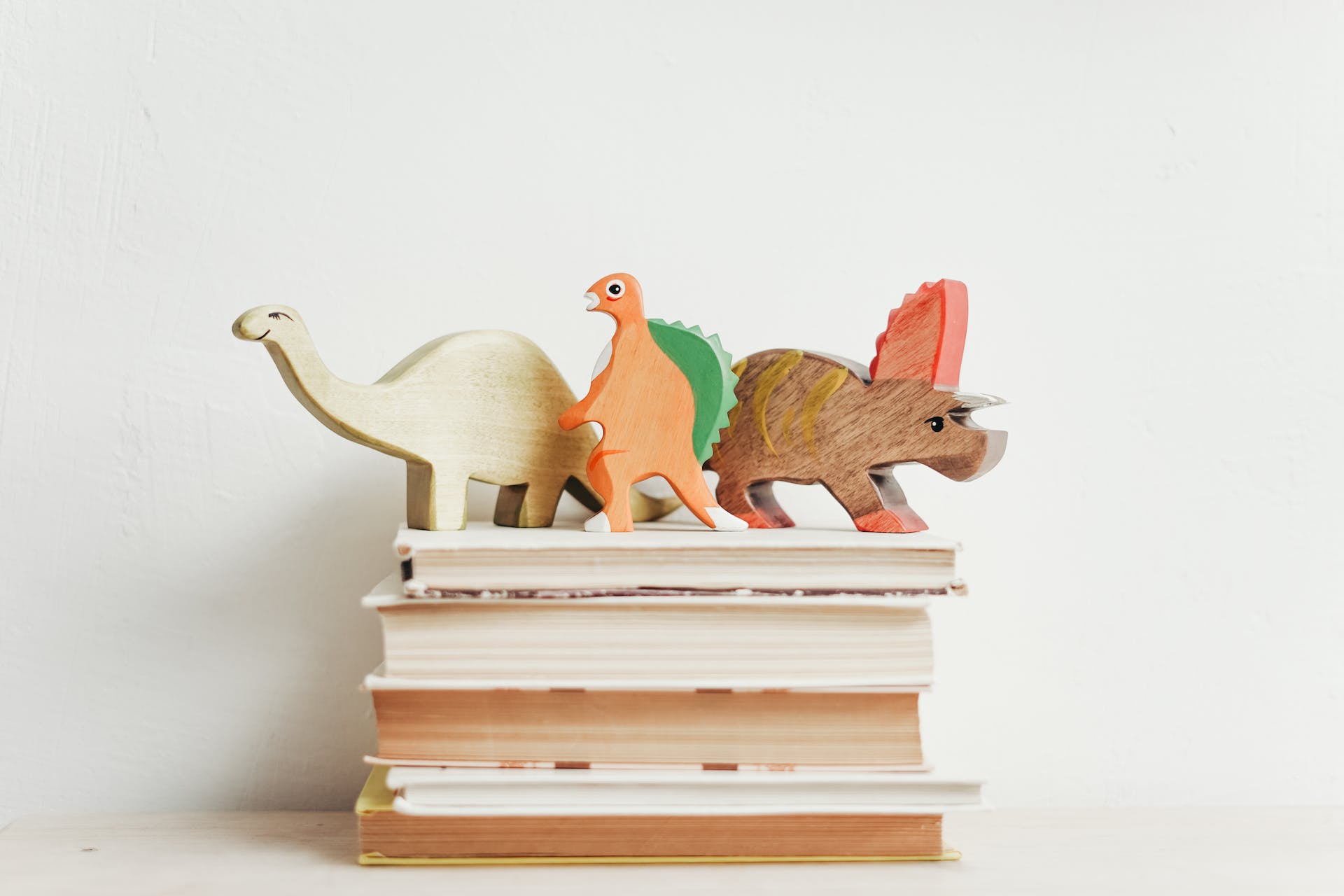 Three wooden dinosaurs stand on top of a stack of books